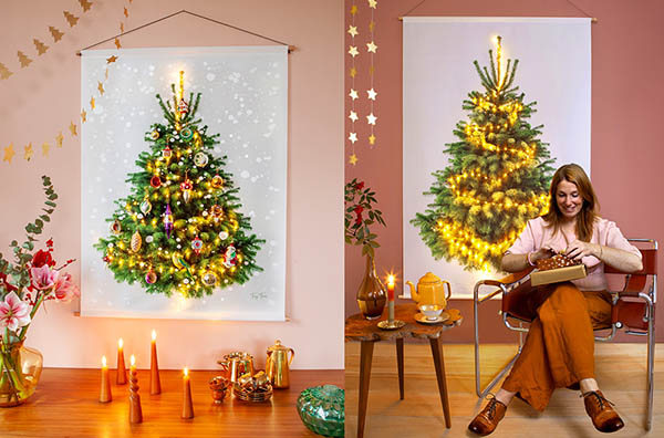 Een grote kerstboom aan de muur met daarvoor een vrouw op een stoel die een cadeautje uitpakt